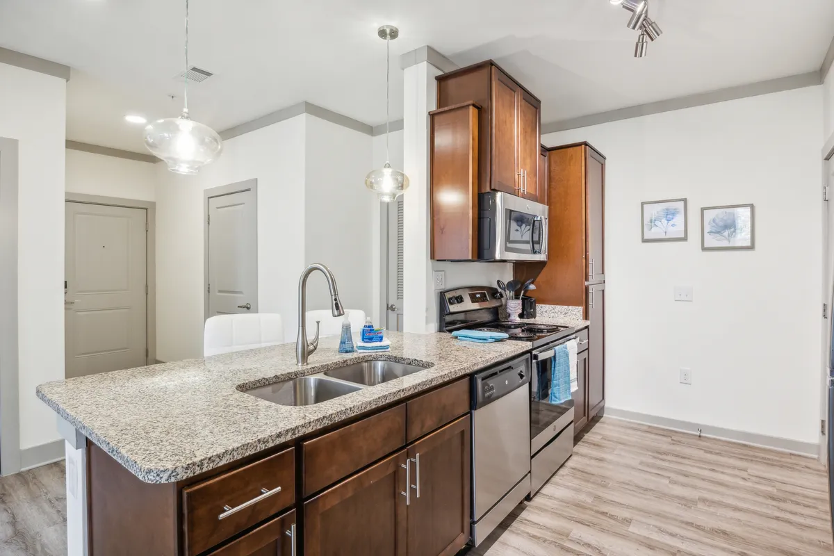 A contemporary kitchen and dining space with granite countertops, stainless steel appliances, pendant lighting, and framed wall art. The scene is set for both everyday living and hosting guests, emphasizing modern elegance and functionality.