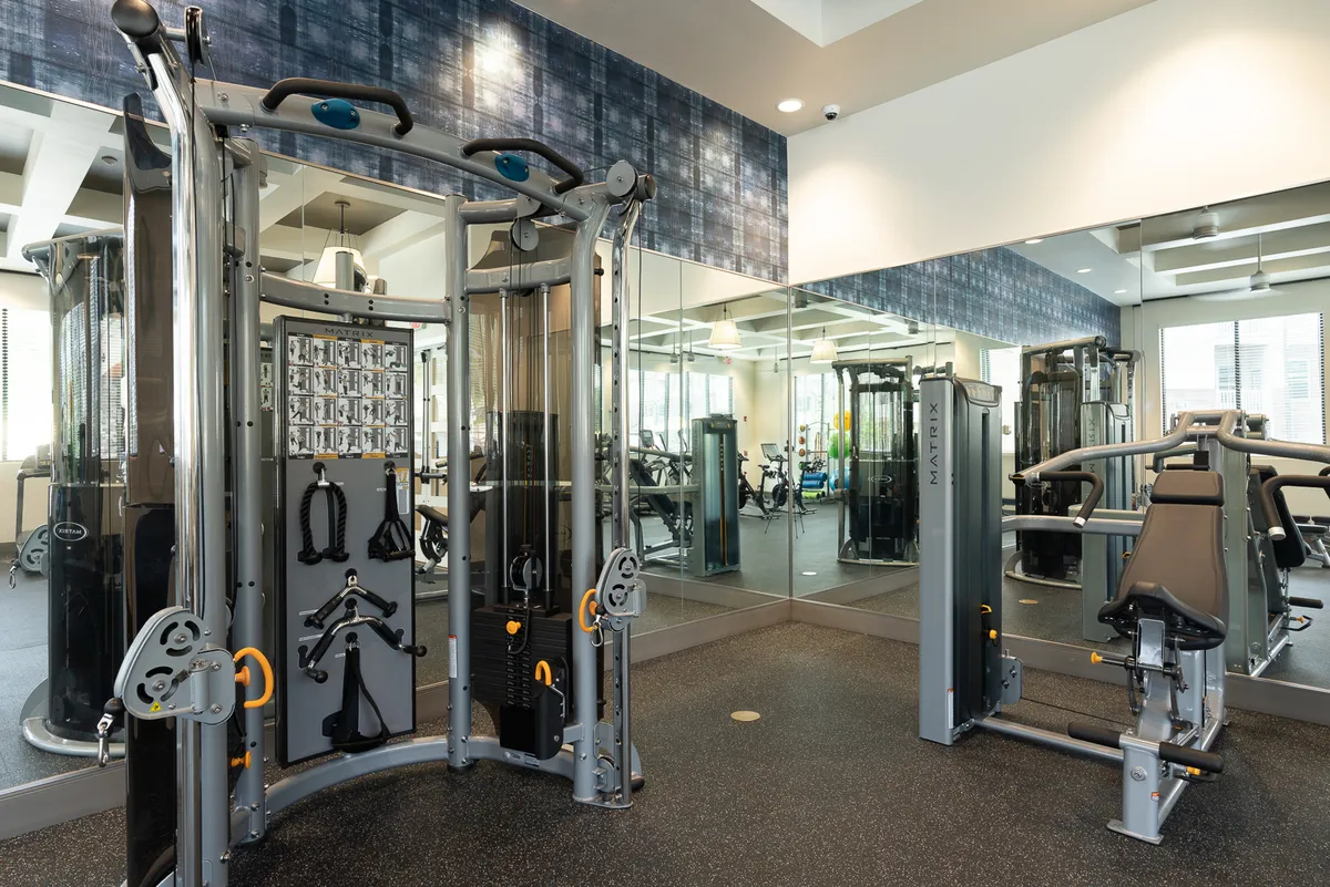 A contemporary fitness room with multi-gym equipment, mirrored walls, and sleek modern design. The setting is dynamic, designed for personal training or group classes, fostering a sense of community and wellness.