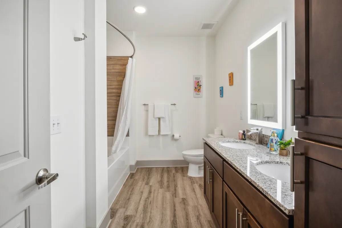 A bathroom with a double vanity, a bathtub with shower curtain, framed mirror, and tasteful wall art. The space is fresh and inviting, designed for both self-care and practical routines.