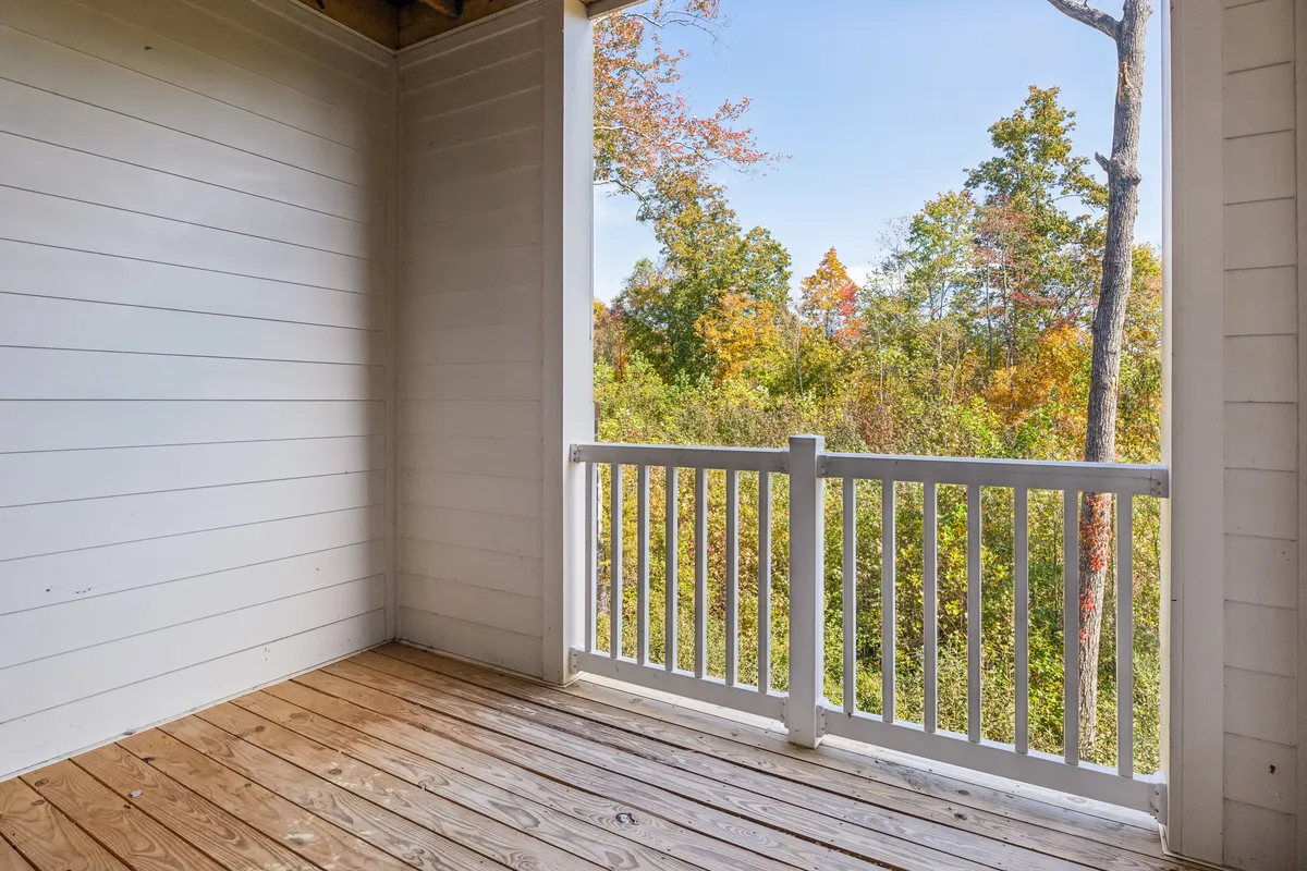 A serene wooden deck with classic white railings overlooks a lush natural landscape. The scene invites a sense of peaceful relaxation, perfect for enjoying a morning coffee or unwinding at sunset. The deck visually connects the comfort of the apartment to the outdoors, evoking the leisurely lifestyle described in the section.