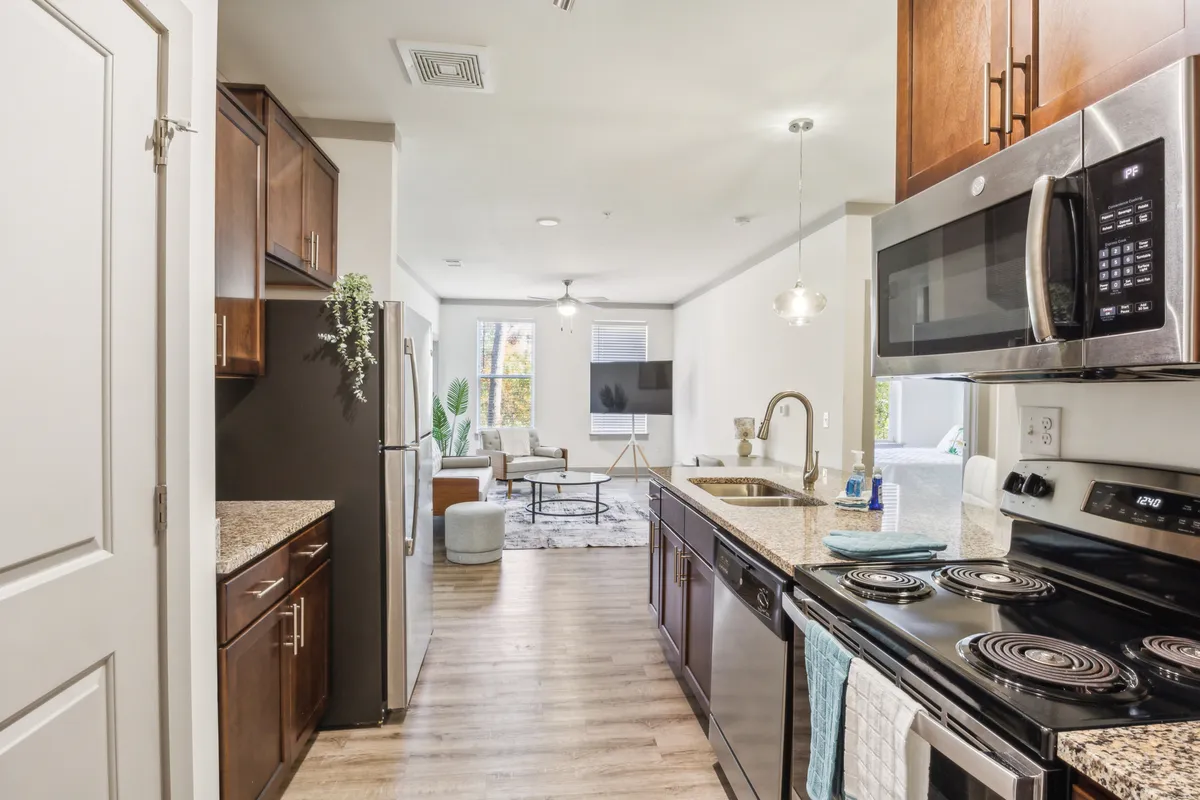 A welcoming kitchen island with stainless steel appliances opens up to a view of the living room, showing a seamless flow between spaces. The area is filled with natural light and exudes a cozy, move-in ready feel.